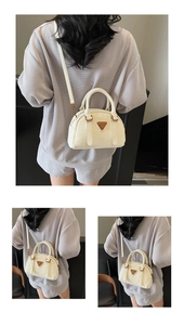 Detail view of a cream Boston bag featuring metallic triangle hardware and crossbody strap