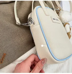 Détail d'un sac à bandoulière crème avec bordure bleue et pendentif en peluche doux