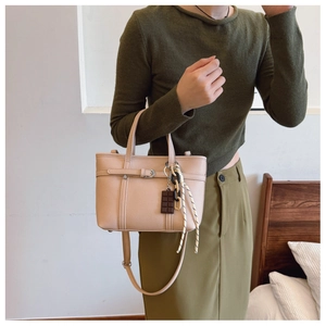 Detail of beige bucket bag with lychee texture featuring a chocolate charm and strap