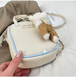Détail du sac en cuir crème à texture litchi avec passepoil bleu et pendentif ours
