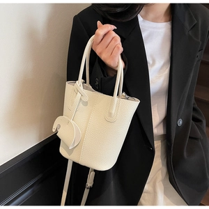 Dettaglio della borsa a secchiello minimalista in pelle crema con grana litchi e tracolla