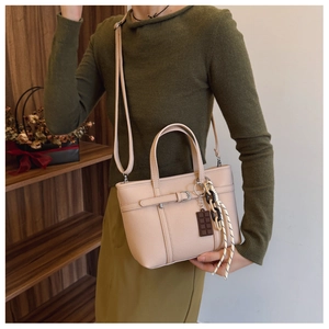 Detail of lychee textured bucket bag in beige with chocolate charm and woven strap