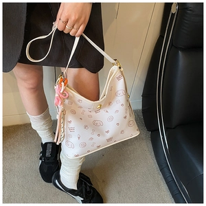 Detalle del bolso hobo blanco con estampados de dibujos marrones y colgante colorido