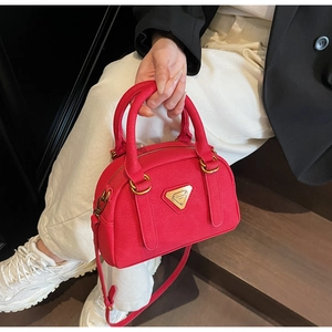 Detail of red Boston bag featuring lychee texture and gold metal plaque with shoulder strap