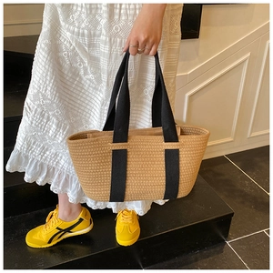 Detalle de bolso de paja tejido con asas negras combinado con un vestido de encaje blanco