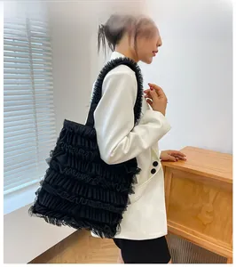 Détail d'un sac cabas en mesh noir à volants texturés porté sur un blazer blanc