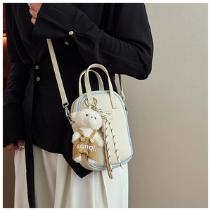Détail du sac crème avec passepoil bleu et pendentif ours en peluche porté à l'épaule