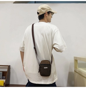 Detail view of mini canvas crossbody phone bag in brown with adjustable strap on male model