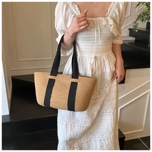 Detalle de bolso cesta de paja tejida con correas anchas de tela negra para estilo playero