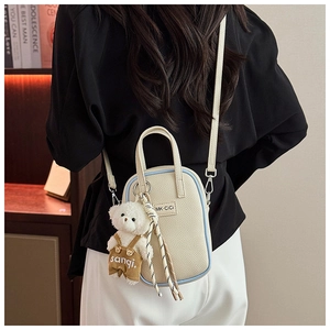 Détail d'un sac bandoulière crème avec breloque ours en peluche et cordon tissé décoratif