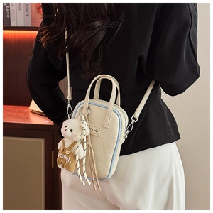 Détail du sac à main crème texturé litchi avec bords bleus et breloque ours doux