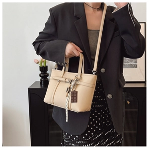 Detail of lychee pattern beige bucket bag featuring a chocolate pendant and woven lanyard