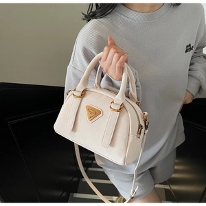 Detail view of cream Boston bag with lychee texture leather and triangular metal plaque
