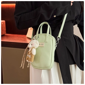 Détail du sac à bandoulière vert clair texture litchi avec un pendentif d'ours mignon