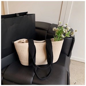 Detalle del bolso tote de algodón tejido beige con asas de lona negra en un banco moderno