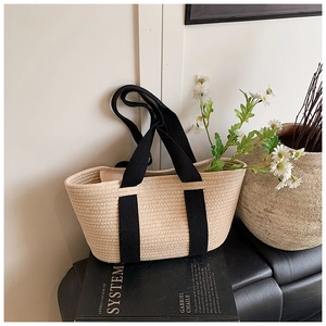 Detalle del bolso tipo tote tejido con asas negras colocado sobre libros y flores