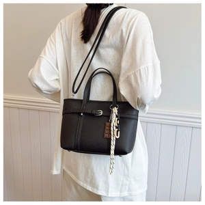 Detail of black lychee grain bucket bag with charm and shoulder strap on model