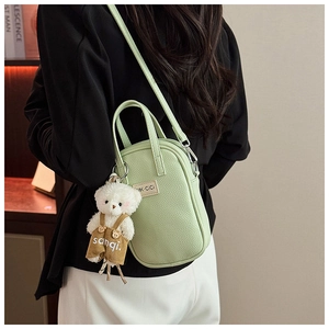 Détail du sac bandoulière vert clair à texture litchi avec un pendentif d'ours blanc