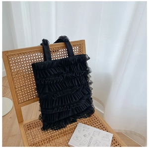 Détail du sac cabas en mesh noir avec volants de dentelle superposés sur une chaise