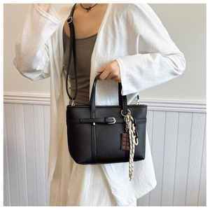 Detail of black lychee texture bucket bag with chocolate charm and woven rope accent