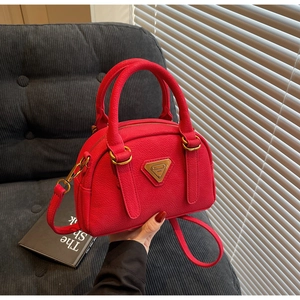 Detail of red lychee grain leather Boston bag with gold triangular metal logo