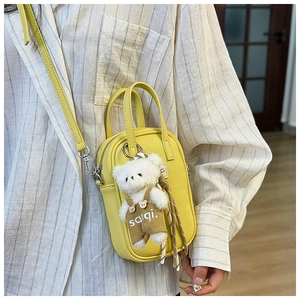 Détail du sac bandoulière jaune texture litchi avec un pendentif d'ours mignon