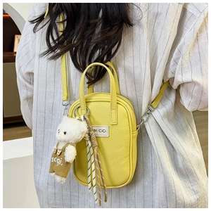 Gros plan d'un sac à bandoulière en cuir jaune grainé avec pendentif ours en peluche