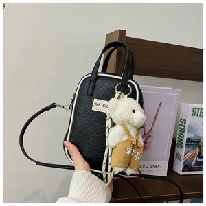 Détail d'un mini sac à main noir à motif litchi avec pendentif ours et logo chic
