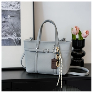 Close-up of light grey litchi leather bucket bag with creative charms and metal hardware