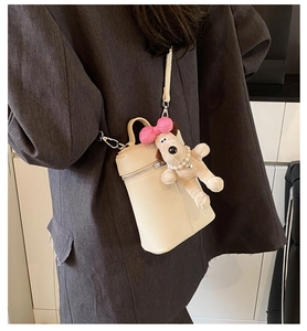 Detail of beige cylinder crossbody bag with lychee texture and cute dog charm accessory