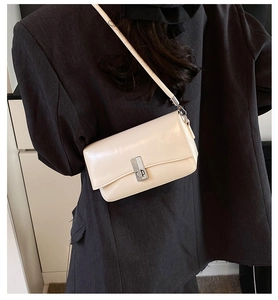 Detail of a beige oil wax leather crossbody bag with silver lock worn over a grey blazer