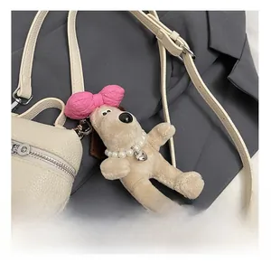 Detail showing a cute plush puppy charm with a pearl necklace on a beige leather handbag