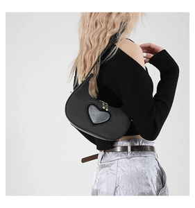 Detail of black crescent shoulder bag with heart patch worn by a model in casual style