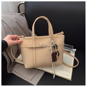 Detail of lychee textured beige bucket bag with decorative scarf and designer charm