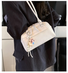 Close-up of a white leather Boston bag with decorative charm worn with a dark blazer