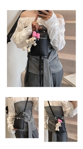 Detail showing a black litchi pattern mini cylinder bag with a plush puppy charm accessory