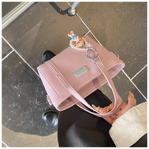 Detailaufnahme der rosa Eimer-Tasche aus Narbenleder mit Namensschild und Puppenanhänger