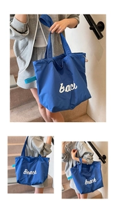 Detail of blue canvas tote bag with white Beach text and side webbing loops