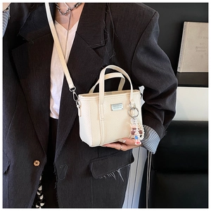 Detailansicht der cremeweißen Eimer-Tasche aus Leder mit Silberlogo und Perlenanhänger