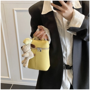 Bright yellow lychee grain leather crossbody bag with a cute plush dog pendant on a model