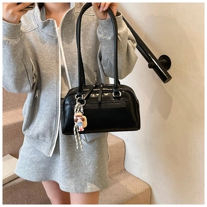 Detail of black PU Boston bag featuring long handles and cute cartoon character charm