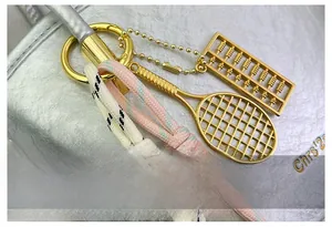 Detail of gold abacus and tennis racket pendants with braided ropes on a texture bag