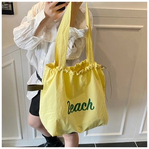 Close-up of drawstring closure and Beach letter print on yellow canvas tote bag