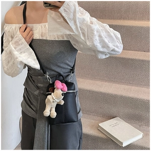 Detail of black lychee grain leather cylinder bag with cute puppy plush charm on staircase