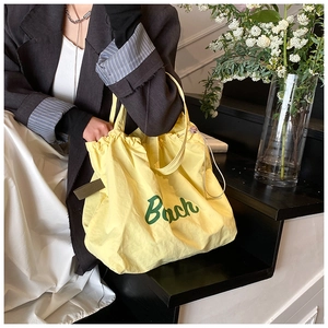 Detail view of bright yellow nylon tote bag with green Bach print and drawstring design