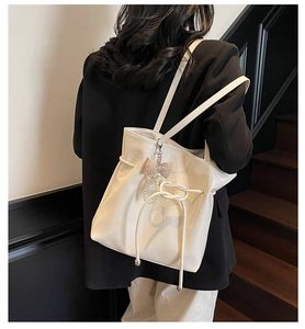 Détail du sac cabas crème avec cuir texturé, nœud coulissant et breloque en perles