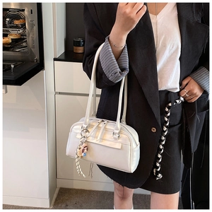 Detail of white Boston bag featuring glossy leather, dual handles and delicate charm