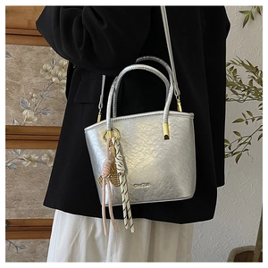Detailed view of silver metallic bucket bag with dual handles and woven rope charms