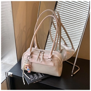 Detailed view of cream Boston bag with dual zippers and a cute doll charm accessory