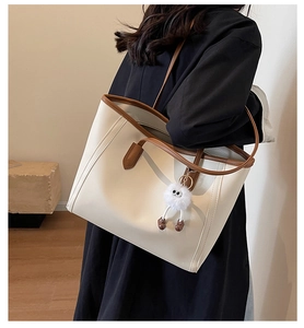 Detail view of contrast stitch tote bag with plush ball charm on model's shoulder